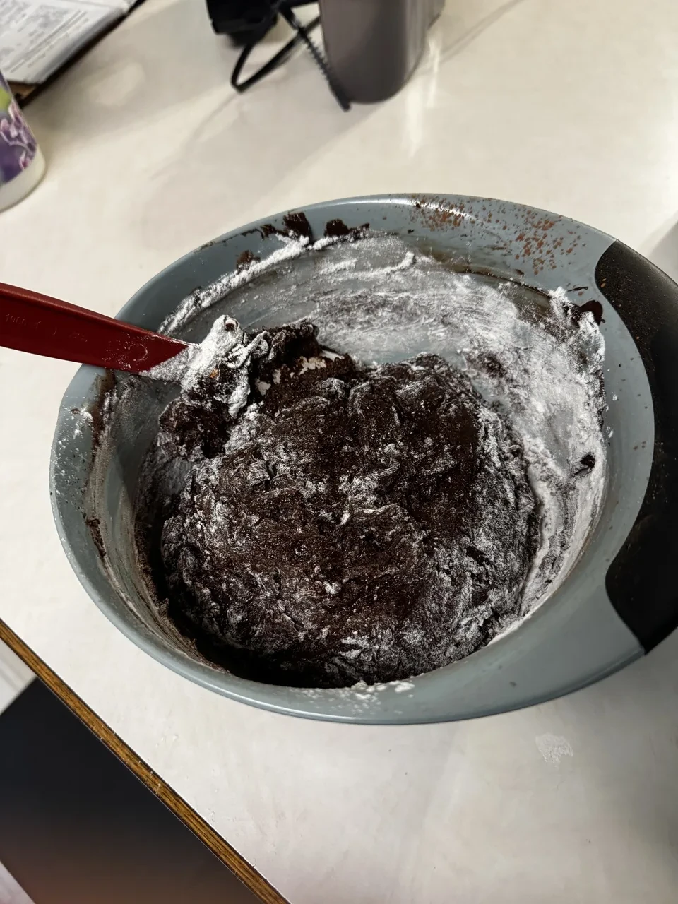 a mixing bowl containing thick chocolate batter with streaks of flour in it