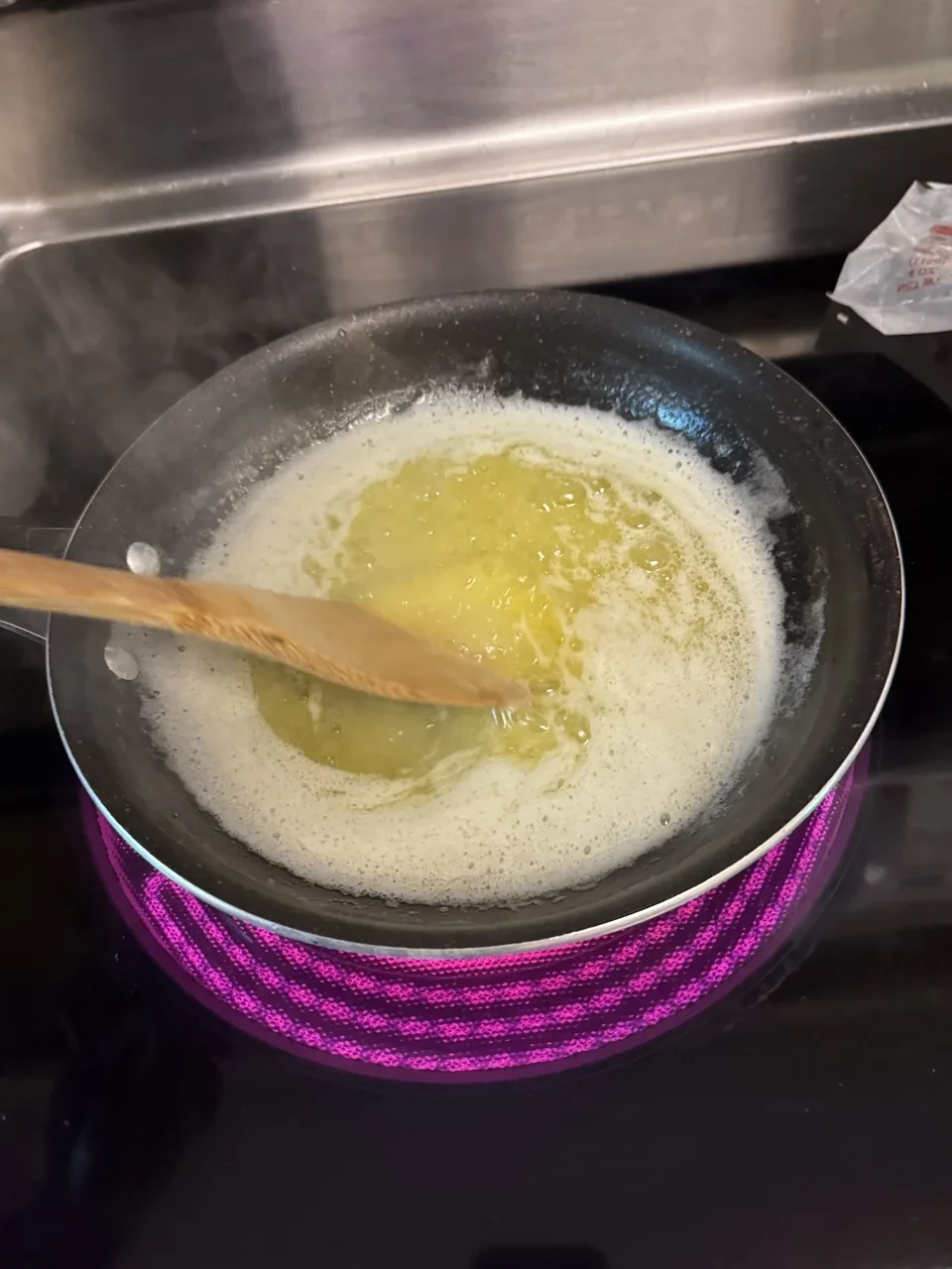 two sticks of partially-melted butter being stirred with a wooden spoon in a saucepan