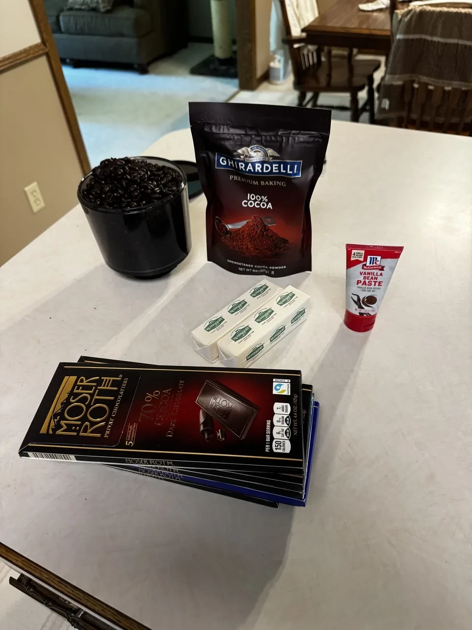 espresso beans, cocoa powder, two sticks of butter, a tube of vanilla bean paste, and six chocolate bars on a countertop