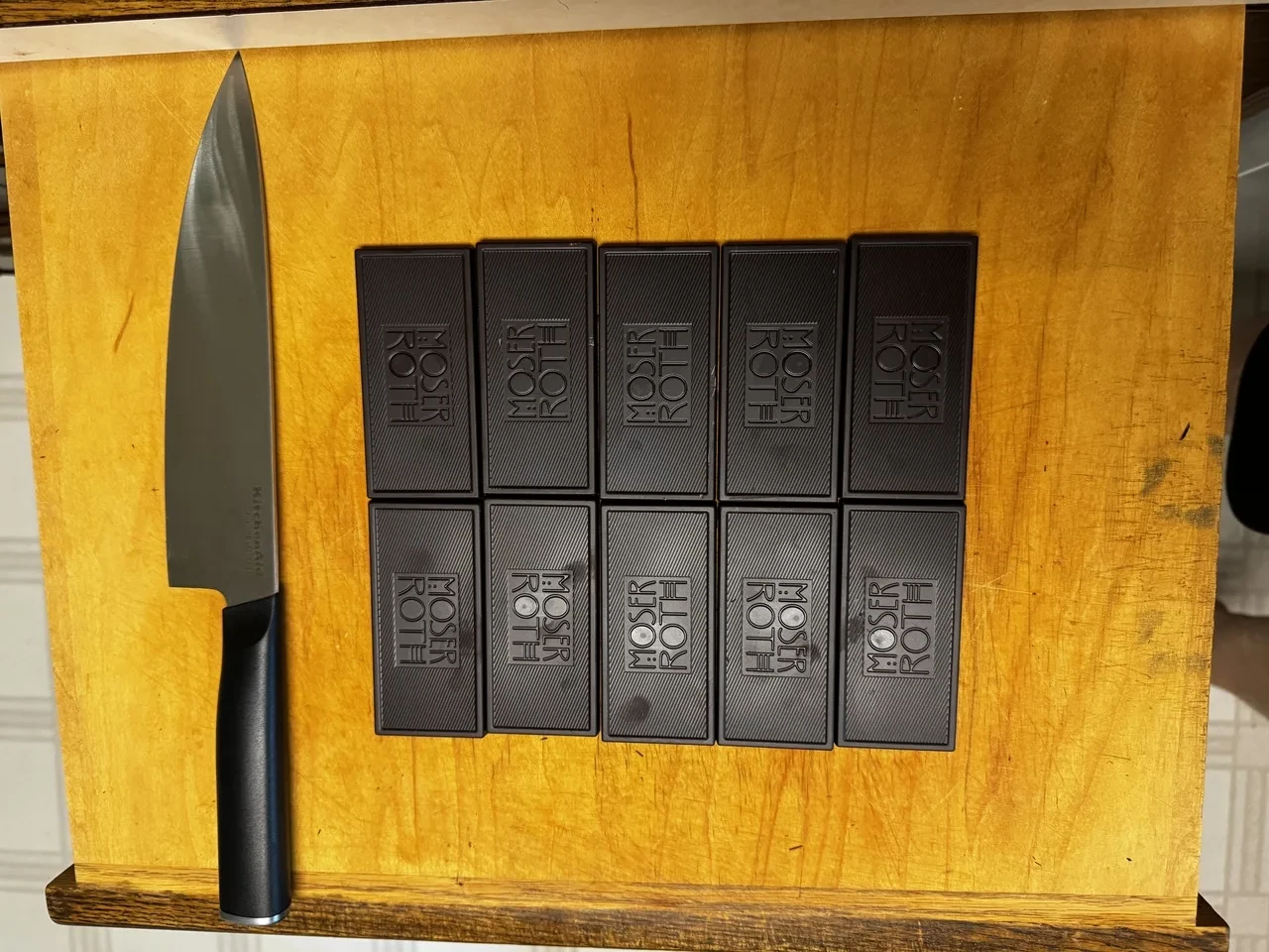 a chef&rsquo;s knife and ten bars of dark chocolate on a wooden cutting board