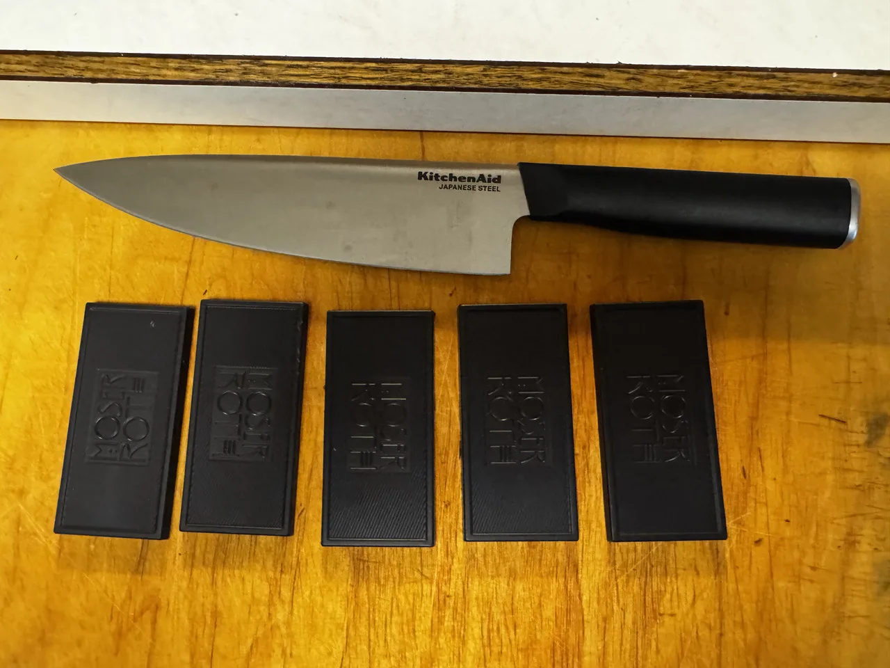 a chef&rsquo;s knife and five dark chocolate bars sitting on a wooden cutting board